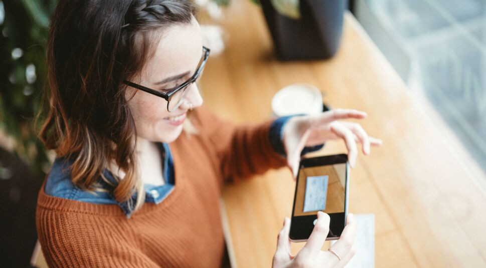 Junge Frau fotografiert ein Dokument via Smartphone ab.