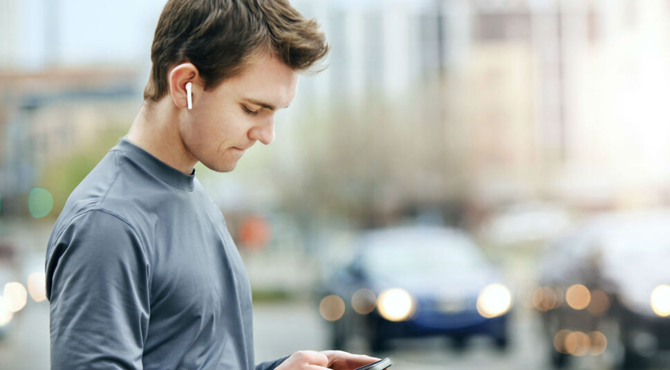 Junger Mann sieht sich auf dem Smartphone den Ladestand seiner AirPods an.