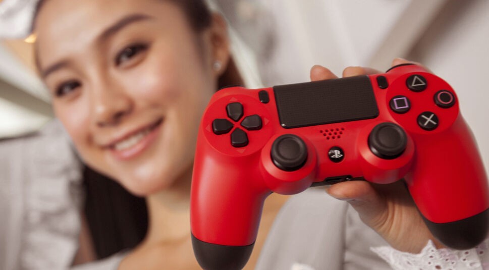 Frau hält einen roten PS4-Controller in die Höhe.
