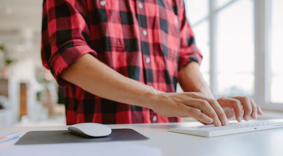 Junger Mann tippt im Büro auf seiner Tastatur.