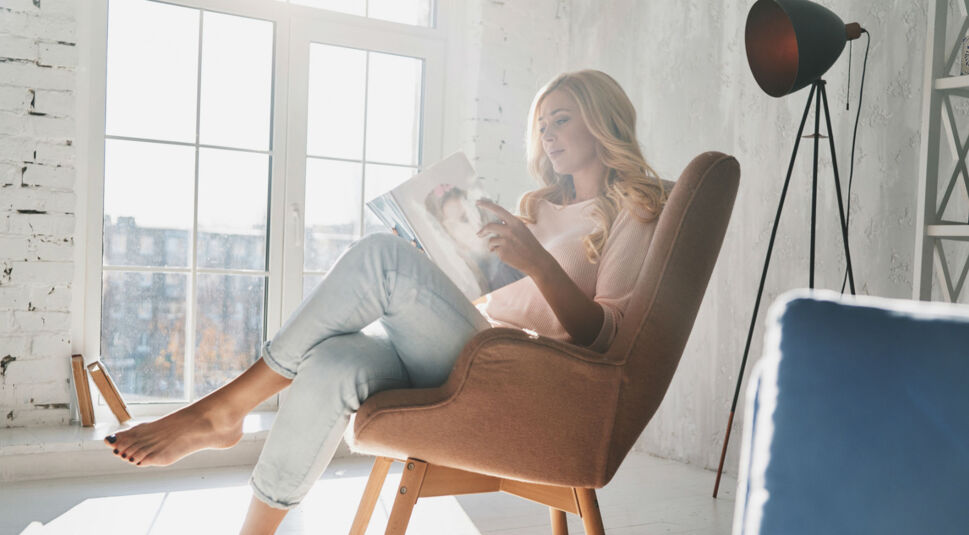Junge Fra sitzt im Stuhl und liest eine Zeitschrift.