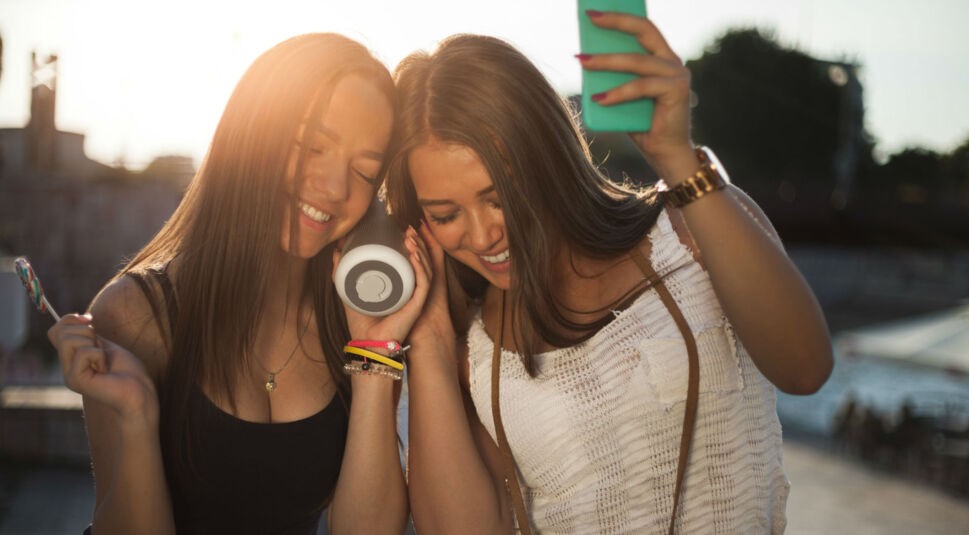 Zwei Freundinnen hören Musik über ihren Lautsprecher.