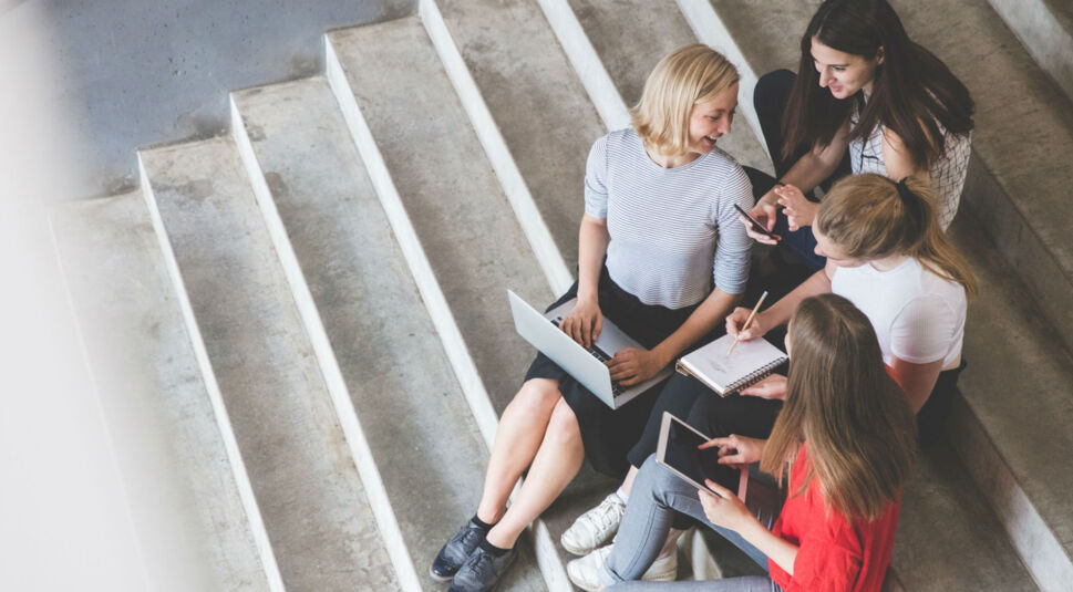 Freundinnen sitzen auf der Treppe und führen einen Gruppenchat auf dem Laptop, Tablet und Smartphone.