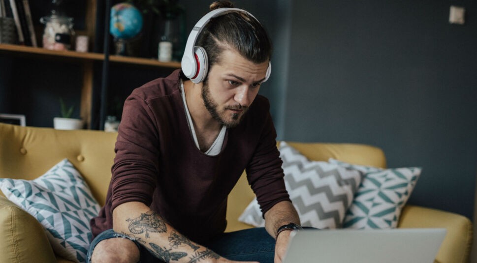 Junger Mann prüft die Audioeinstellungen seines Laptops.
