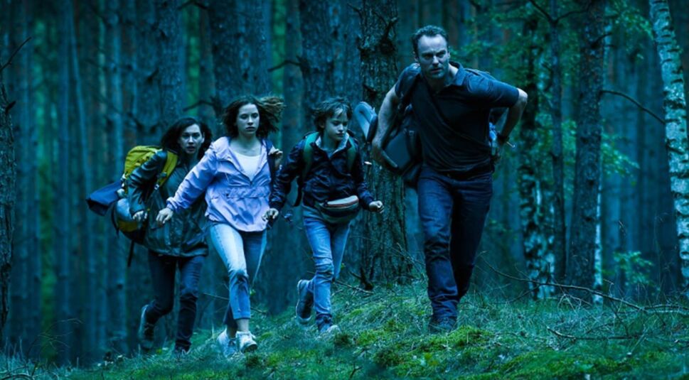 Das Bild zeigt eine Familie die durch den Wald läuft.