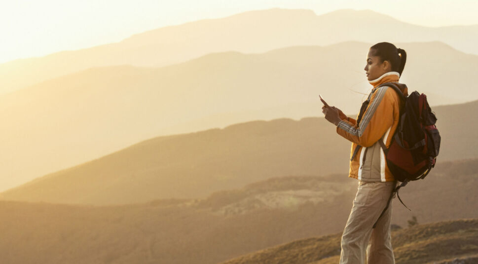 Junge Frau nutzt ihr Smartphone beim Wandern in den Bergen.