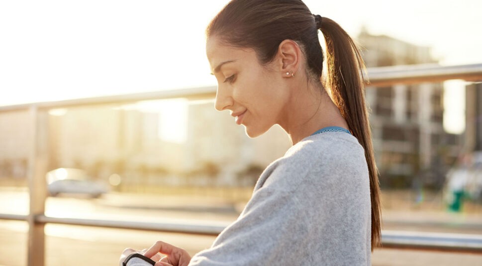Junge Frau tippt auf das Display ihres Fitbit-Trackers.