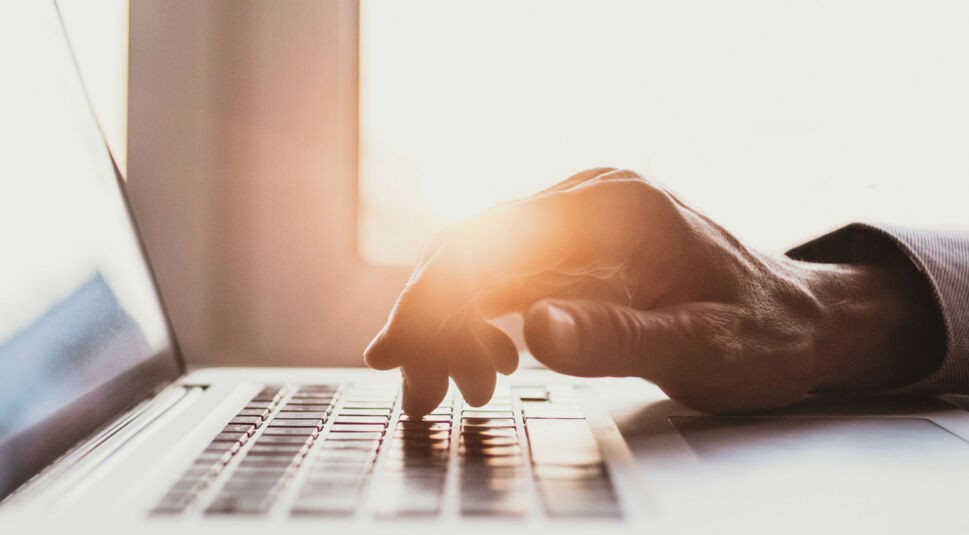 Junger Mann tippt am Laptop.