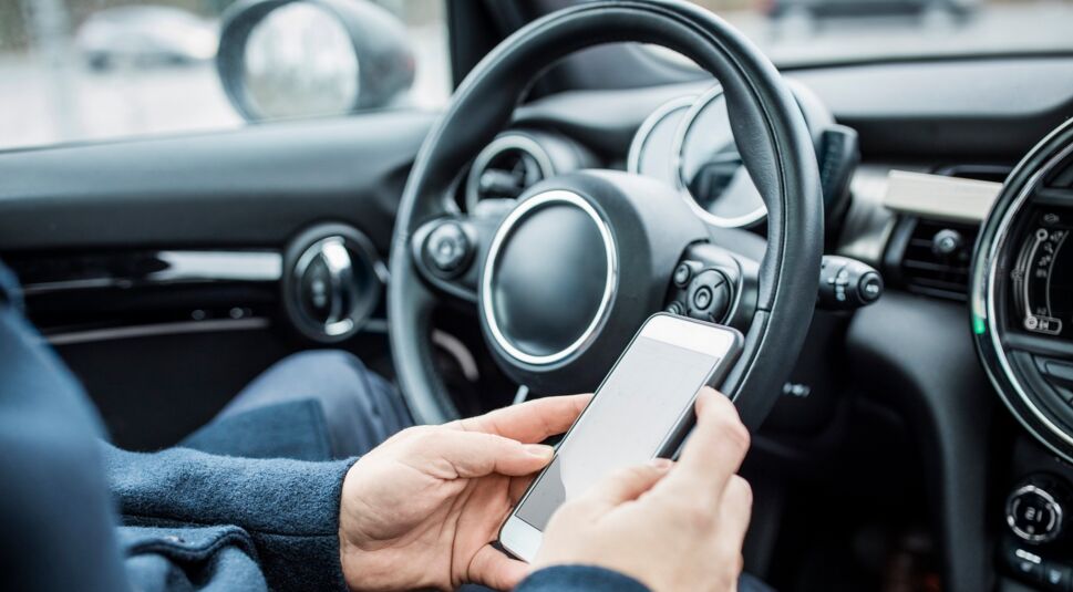 Ein junger Mann entsperrt über sein Smartphone das per Carsharing-App gebuchte Auto.