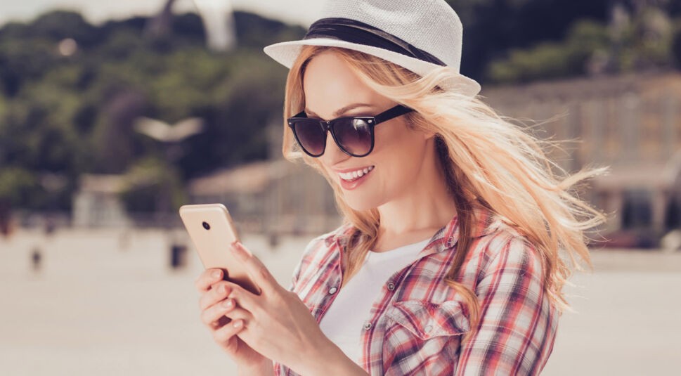 Junge Frau lächelt ihr Smartphone an, auf dem Threema installiert ist.