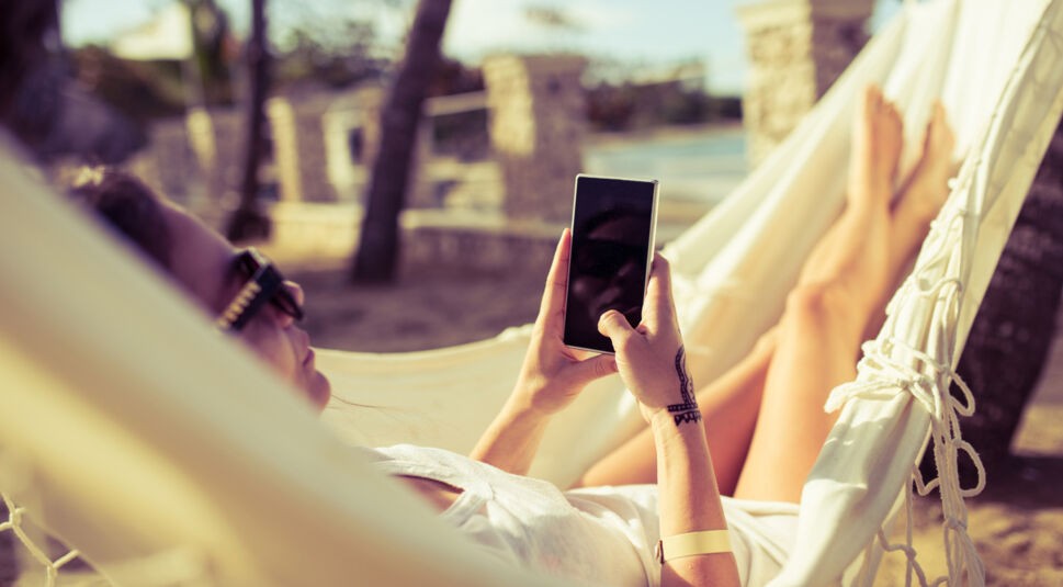 Frau entspannt in ihrer Hängematte am Strand und nutzt Lese-Apps