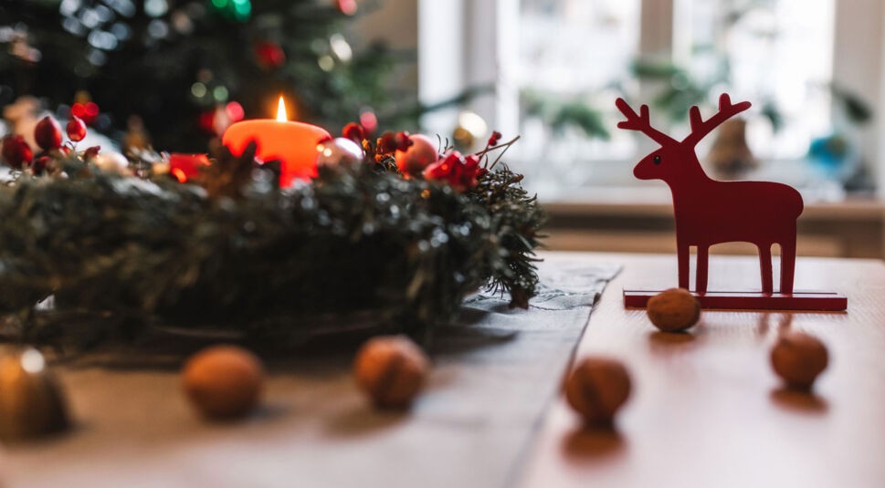 Ein Adventskranz auf einem Tisch, daneben ein rotes Rentier.