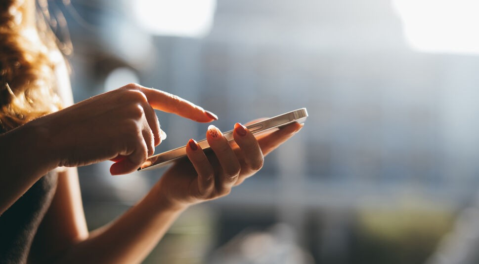 Zu sehen ist der Oberkörper einer Frau, die etwas auf ihrem Smartphone auswählt.