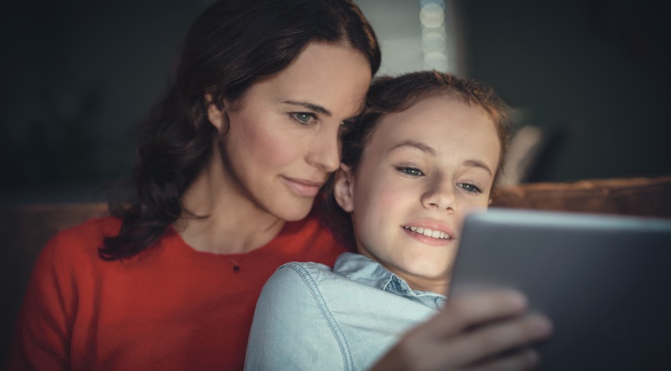Eine Mutter schaut ihrer Tochter über die Schulter, die sich etwas am Tablet ansieht.