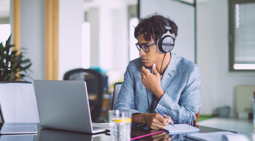 Ein junger Mann trägt Kopfhörer beim Arbeiten am Laptop.