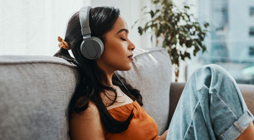 Frau hört mit geschlossenen Augen und Kopfhörern Wissens-Podcasts