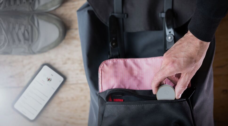 In einen Rucksack wird der Curve GPS Tracker von Vodafone eingepackt, daneben liegt ein Handy und Wanderschuhe.