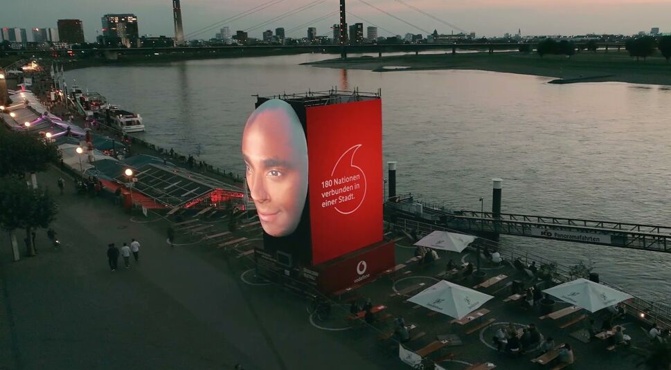 Die Kunst-Installation "Faces of Düsseldorf", zu sehen ist ein projiziertes Gesicht, daneben eine LED-Animation. Im Hintergrund ist der Rhein zu sehen.