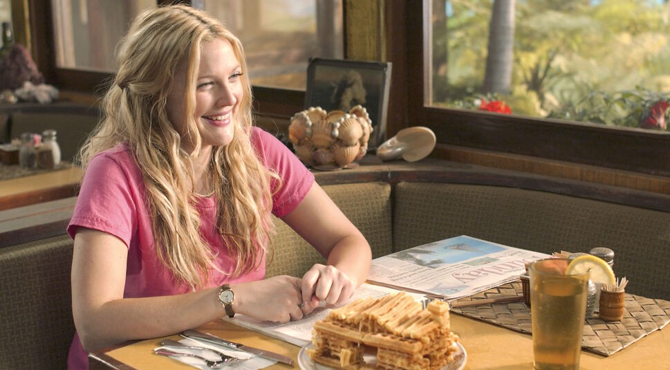 In einer Szene aus 50 erste Dates, einem von Drew Barrymores besten Filmen, sitzt sie in einem hawaiianischen Diner und lacht strahlend. Sie trägt ein pinkes T-Shirt, hat wellige blonde Haare und wirkt fröhlich. Vor ihr auf dem Tisch steht ein Getränk mit Zitronenscheibe und ein Frühstück aus Waffeln, geformt wie eine kleine Hütte.