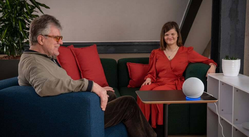 Ein Mann und eine Frau hören einem Audio-Inhalt über ihr Alexa-Gerät auf dem Wohnzimmertisch zu.