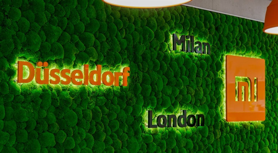 Eine grüne Wand im Xiaomi-Office in Düsseldorf, zu lesen sind die Städtenamen "Düsseldorf", "Milan" und "London".