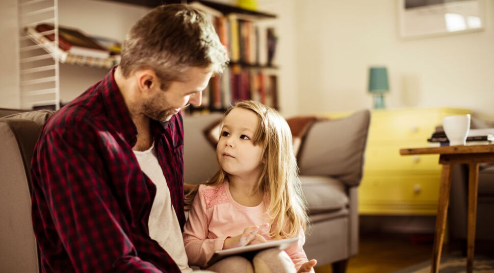 Vater schaut mit seinem Kind auf ein Tablet.