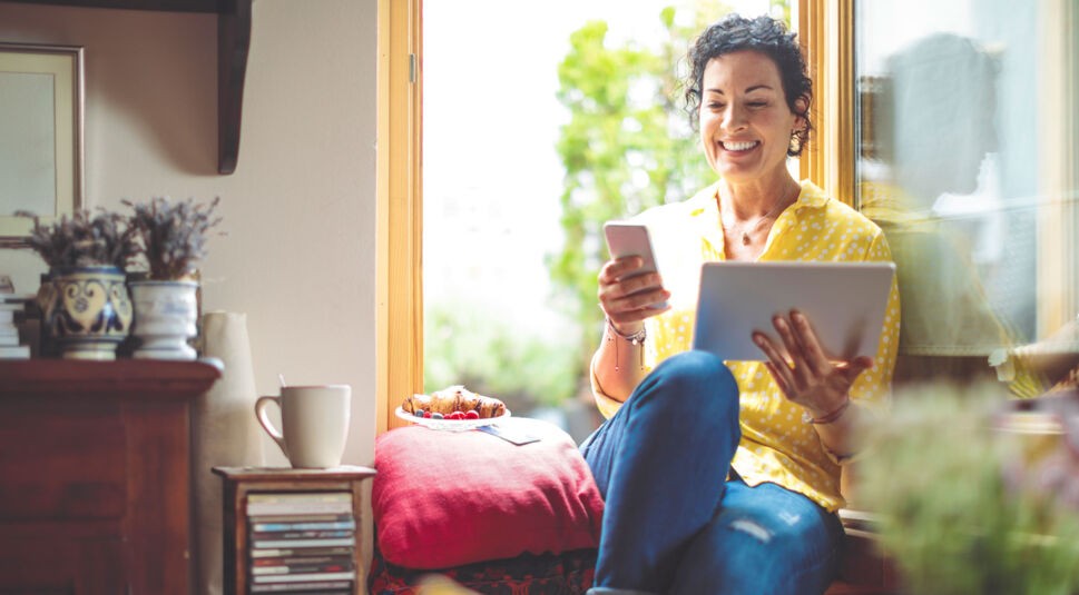 Eine Frau sitzt an einem Fenster und hält ihr Smartphone in der Hand