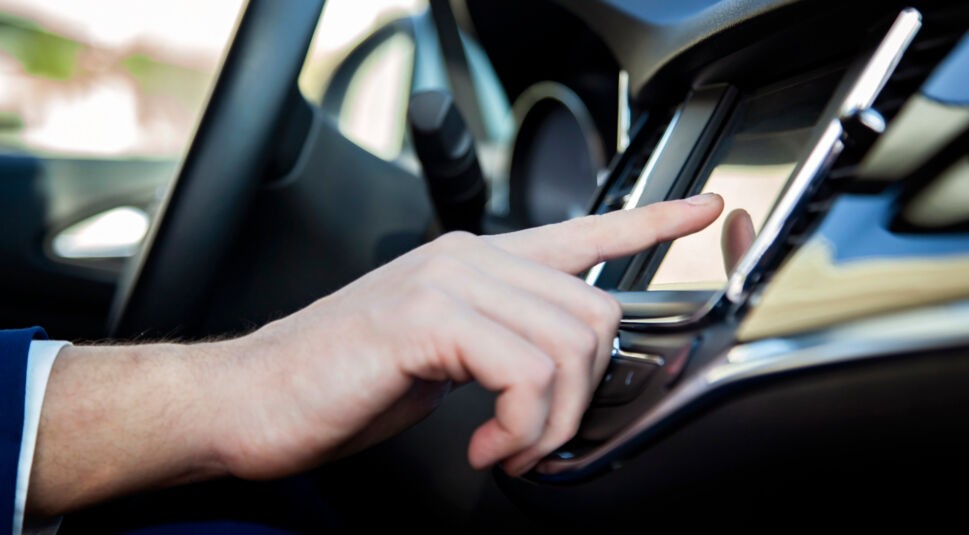 Person tippt im Auto auf das Display des Infotainmentsystems