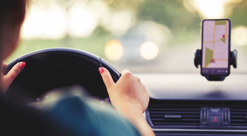 Frau fährt mit dem Auto, nutzt Google Maps auf dem Handy