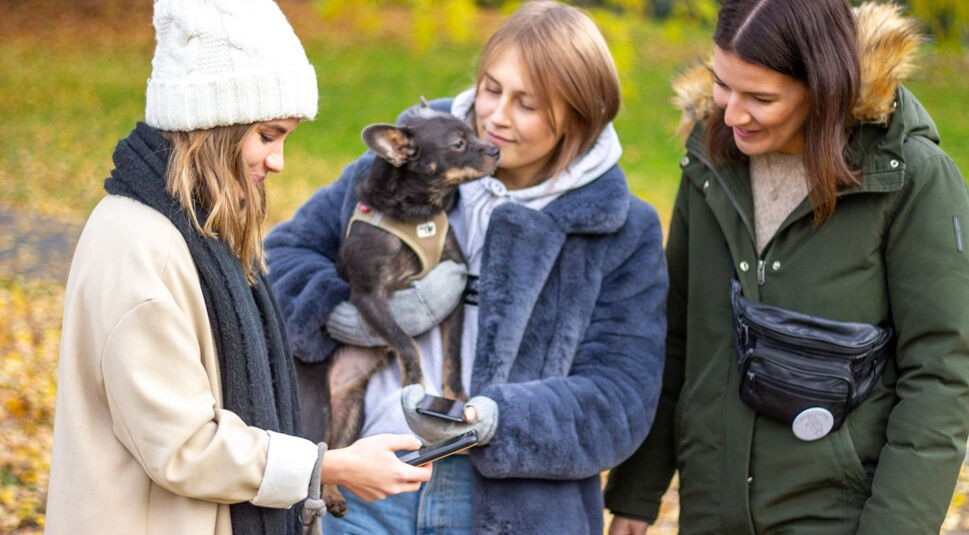Drei Mädchen stehen draußen zusammen, eine trägt einen Hund auf dem Arm.