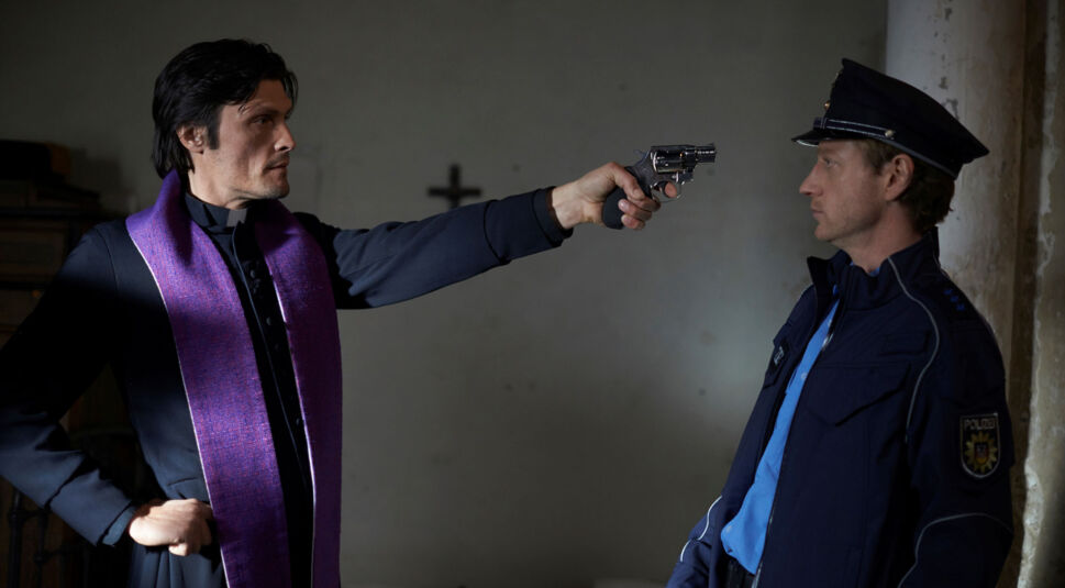 Ein Priester bedroht einen Polizisten mit einer Waffe