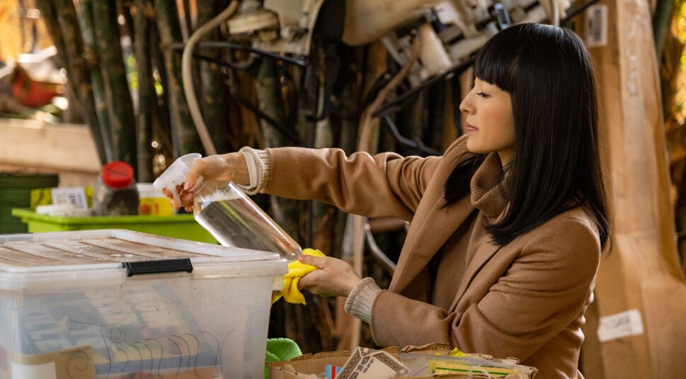 Marie Kondo reinigt mit einer Sprayflasche eine Oberfläche, vor ihr steht eine Kiste.