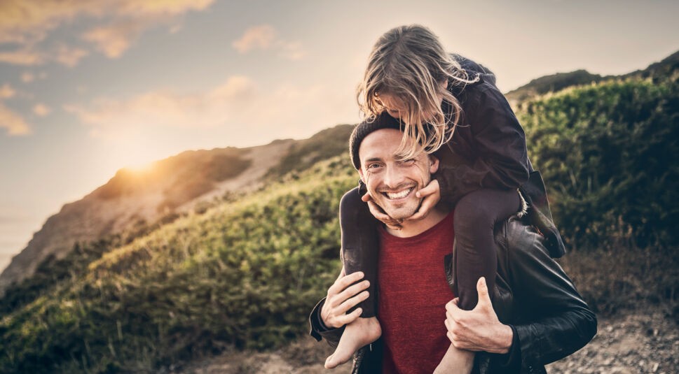 Ein Vater trägt seine Tochter auf den Schultern, sie stehen an einem Berg.