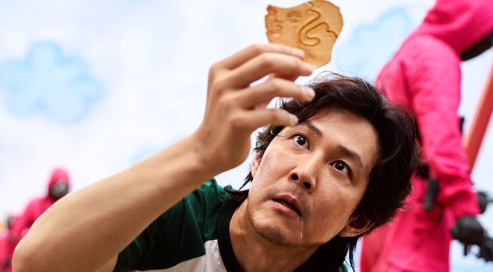 Der Spieler Seong Gi-hun (Lee Jung-jae) hält in der Netflix-Serie "Squid Game" einen Keks hoch.