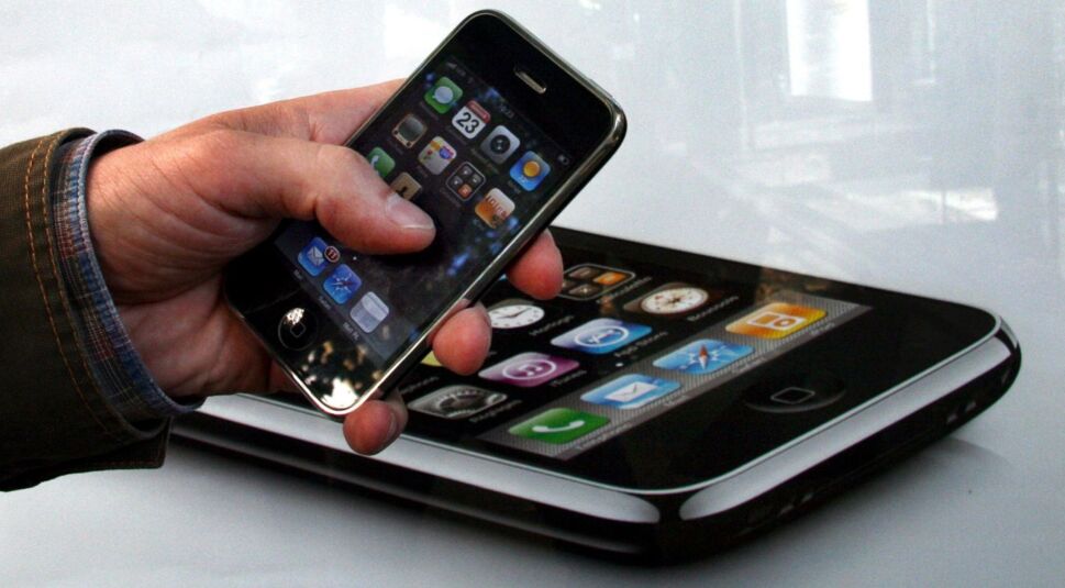 Hand hält iPhone 3GS vor Plakat mit gleichem Modell