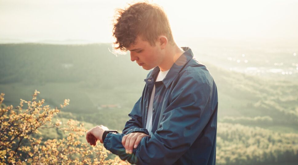 Junger Mann schaut auf seine Smartwatch.