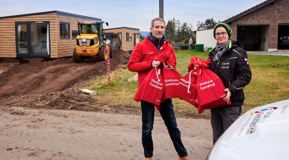 Zwei Vodafone-Mitarbeiter:innen stehen vor Tiny Houses im Ahrtal, die mit Internet und TV von Vodafone ausgestattet werden.