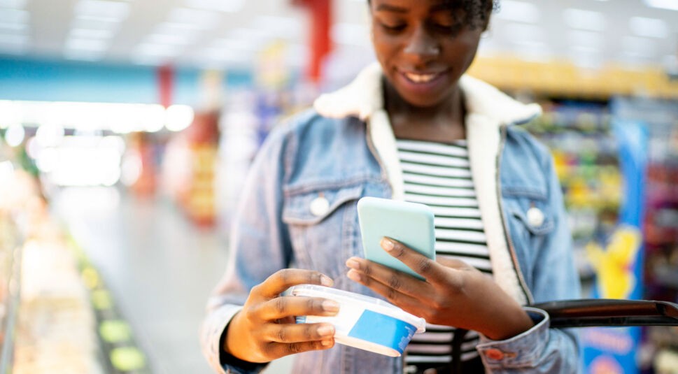 Frau mit Smartphone im Supermarkt nutzt smarte Einkaufslisten