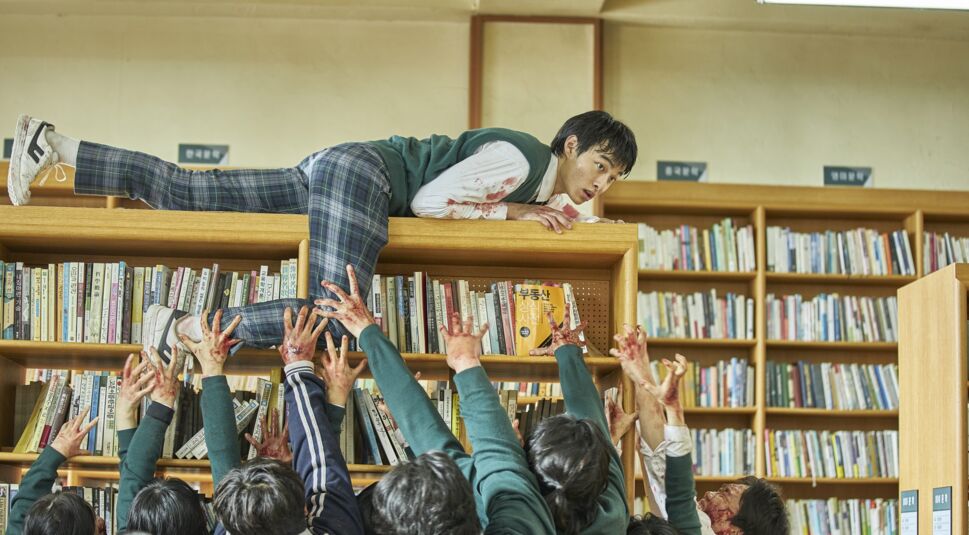 Ein Mann rettet sich vor einer Zombiehorde auf einen Schrank.