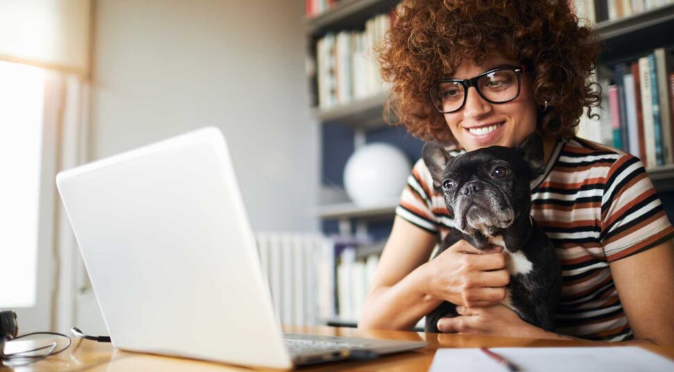 Eine Frau sitzt mit ihrem Hund vor hrem Laptop und freut sich