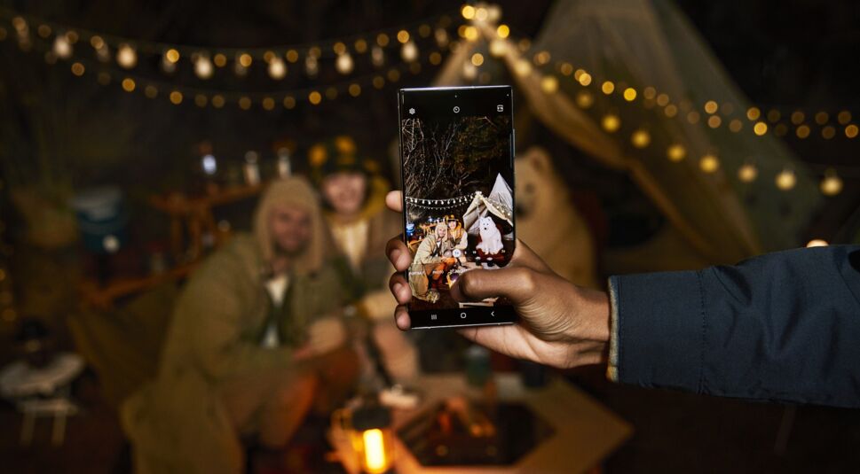Hand hält Smartphone Galaxy S22 Ultra, das bei Nacht eine fröhliche Gruppe fotografiert
