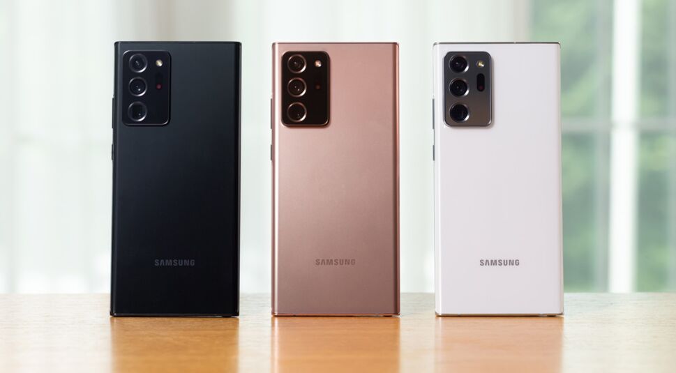 Drei Smartphone-Rückseiten in verschiedenen Farben des Galaxy Note20 Ultra nebeneinander auf Holztisch