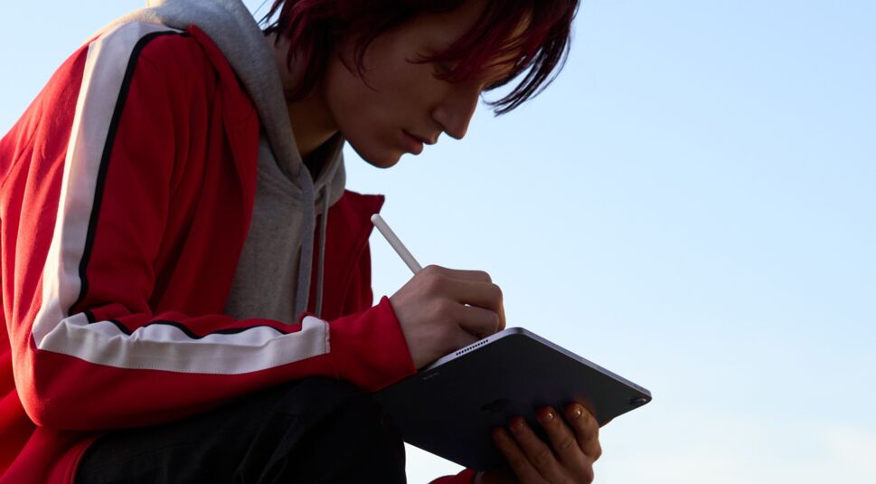 Junger Mann mit roter Jacke auf Skateboard schreibt mit Apple Pencil auf iPad Air 5