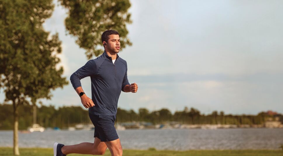 Mann mit Smartwatch Fitbit Versa 3 rennt am Ufer eines Sees