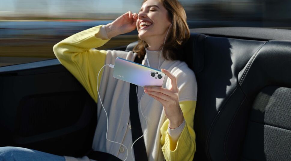 Lachende Frau im Auto auf Rückbank hört Musik mit dem Smartphone OPPO Reno8 Lite 5G