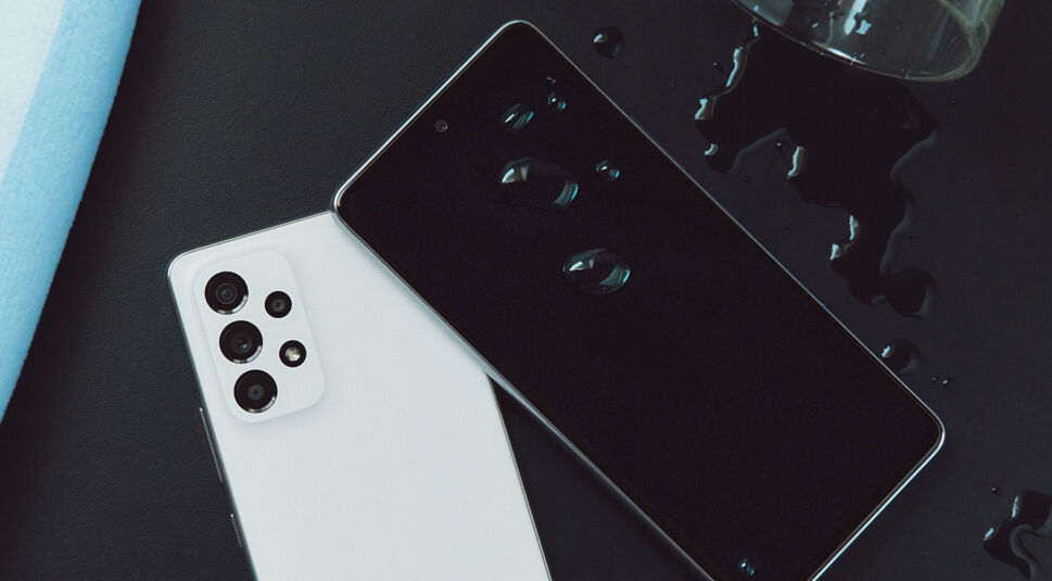 Smartphone Galaxy A53 in Schwarz und Weiß auf einem Tisch mit Wasser darüber aus einem Glas