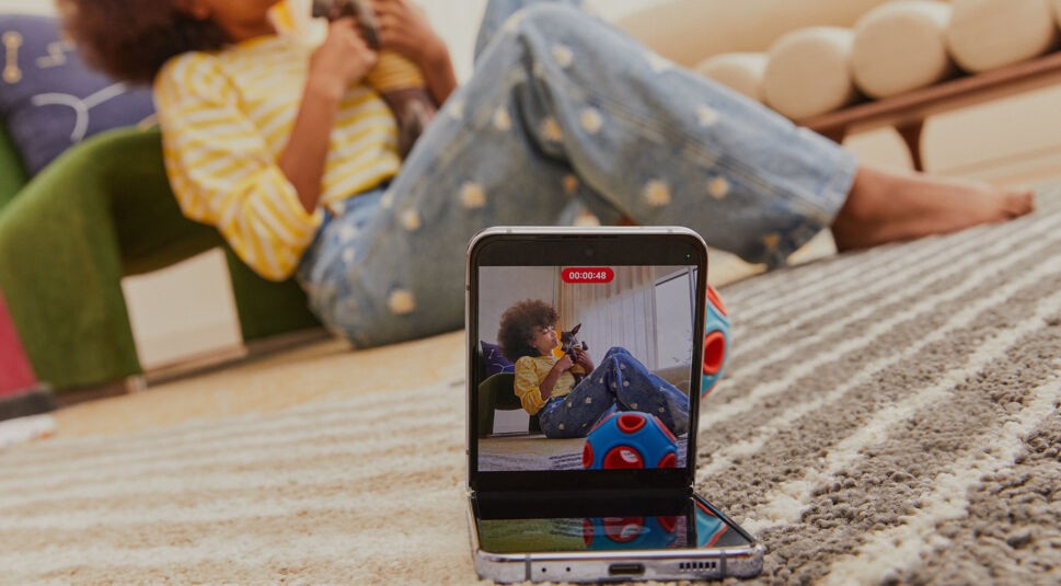 Im Vordergrund Galaxy Z Flip4, auf dem Display Frau mit Katze, die im Hintergrund auf dem Boden sitzt