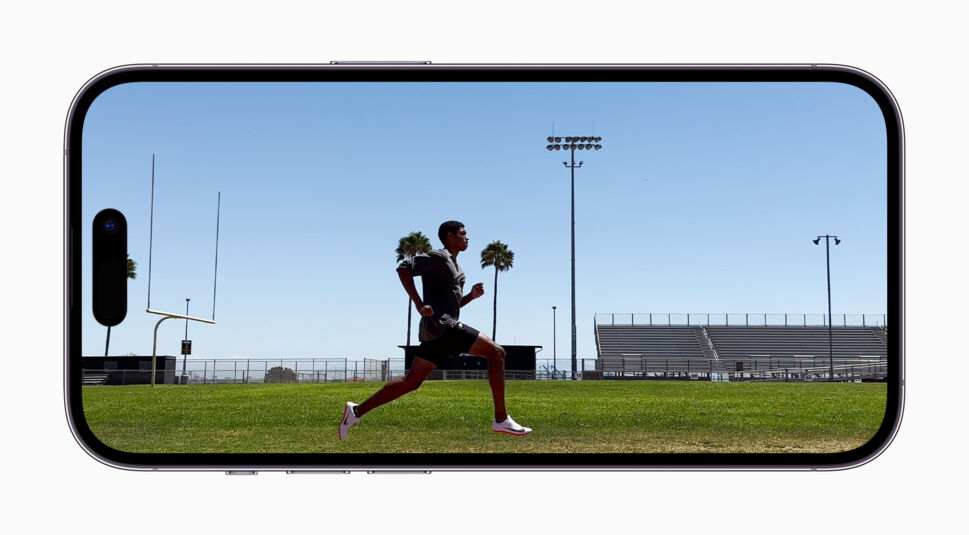 iPhone 14 Pro Max Display zeigt Läufer von der Seite auf einem Sportplatz mit Palmen