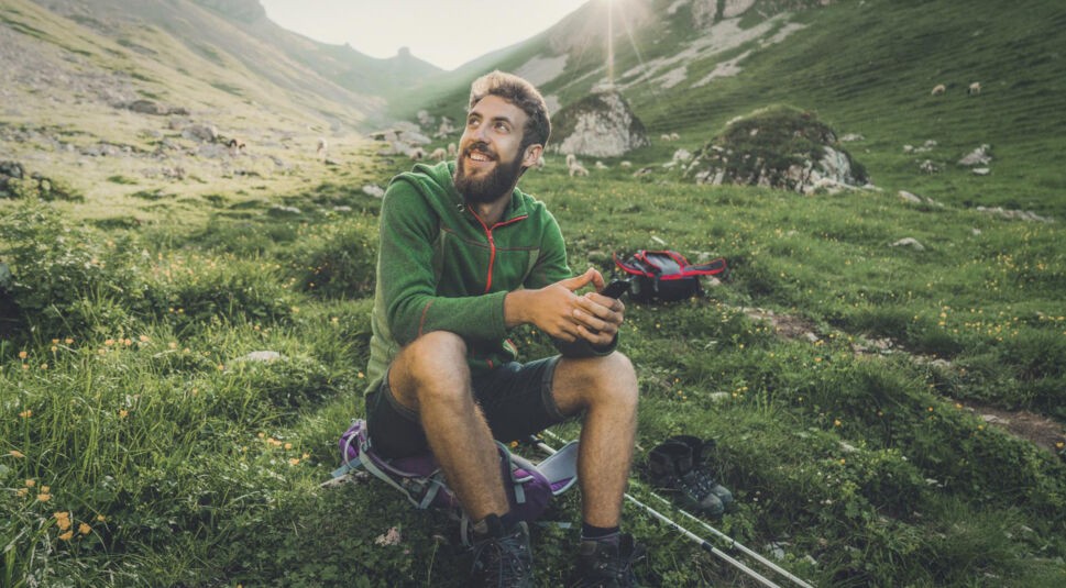 Mann sitzt mit Handy in Natur