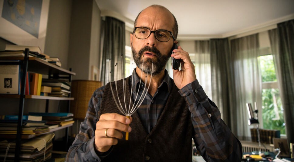 Christoph Maria Herbst schaut auf ein Kopf-Massagegerät